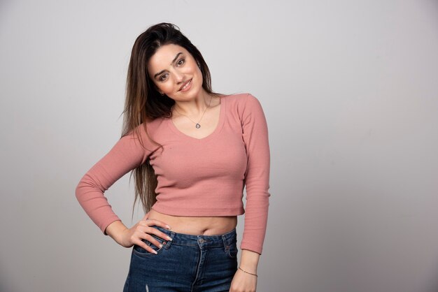 A beautiful young woman with long hair standing with hand on hip . 