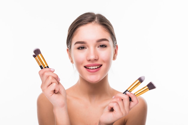 Beautiful young woman with makeup brushes near her face isolated on white wall