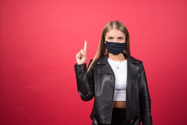 Beautiful young woman with a medical face mask pointing up