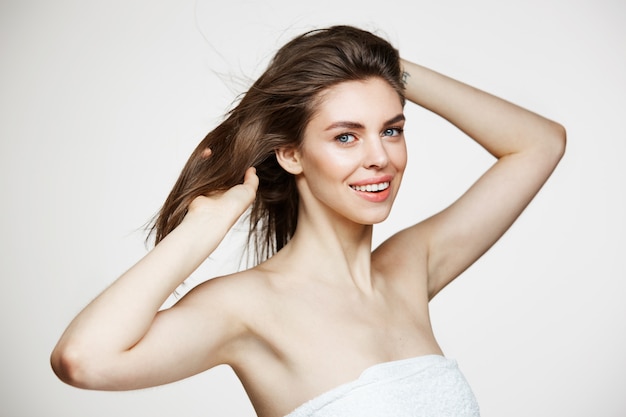 Free photo beautiful young woman with perfect clean skin smiling touching hair over white wall. facial treatment.