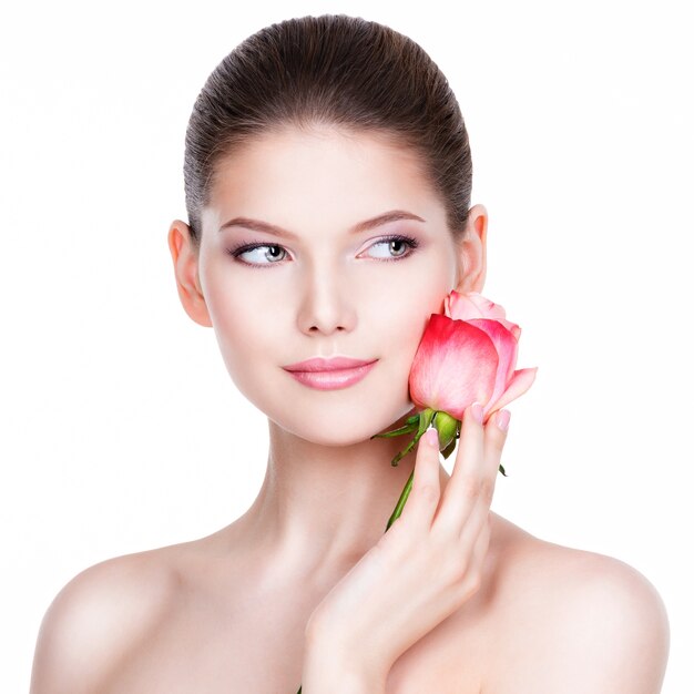 Beautiful young woman with pink rose. Beauty treatment concept. Portrait over white wall.