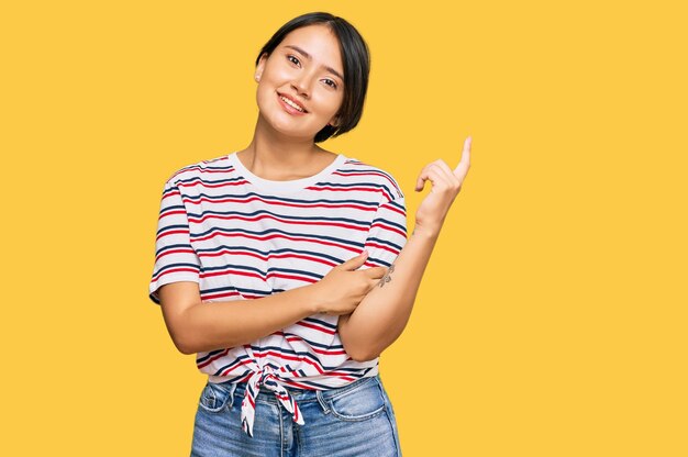 Beautiful young woman with short hair wearing casual clothes with a big smile on face pointing with hand and finger to the side looking at the camera