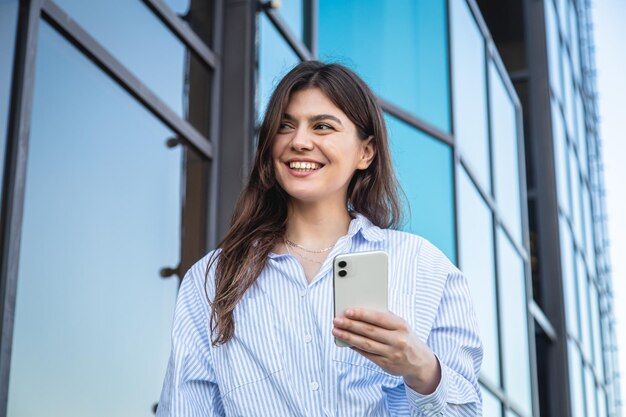 ガラスの建物の背景にスマートフォンを持つ美しい若い女性