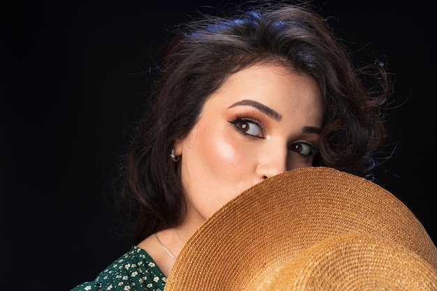 Free photo beautiful young woman with straw hat posing against black background