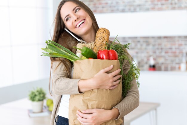 美しい若い女性は野菜を食卓の袋に入れて家にいます。