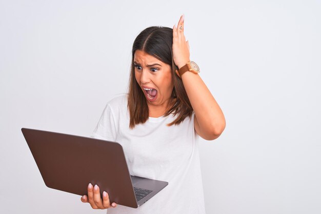 Beautiful young woman working using computer laptop over white background Crazy and scared with hands on head afraid and surprised of shock with open mouth