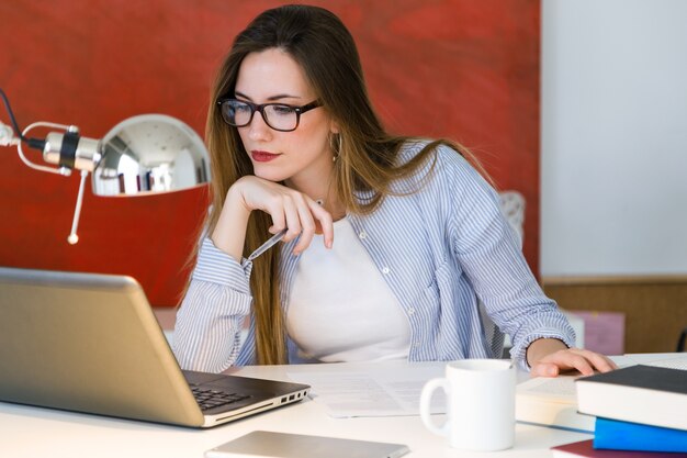 아름 다운 젊은 여자는 그녀의 사무실에서 노트북으로 작업.