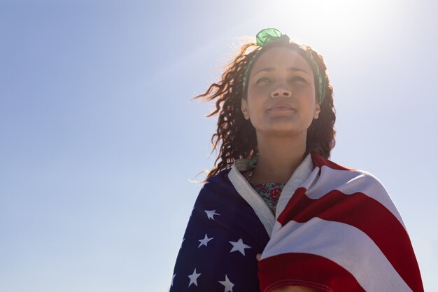 日差しの中でビーチにアメリカ国旗に包まれた美しい若い女性