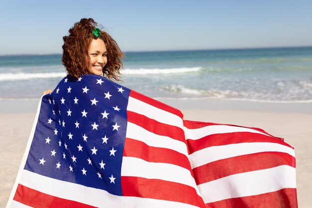 햇빛에 해변에서 카메라를 찾고 미국 국기에 싸여 아름 다운 젊은 여자