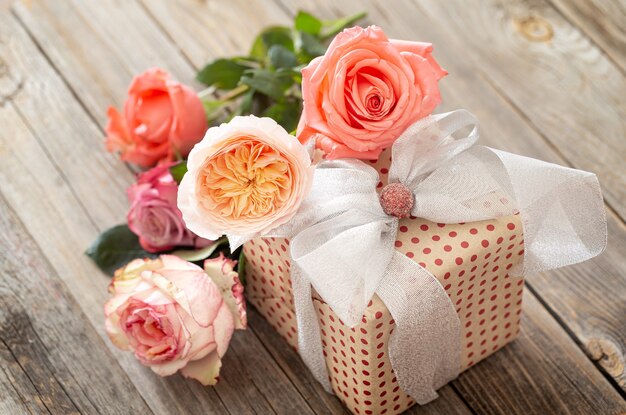 Beautifully wrapped gift and a bouquet of roses on a blurred wooden table.