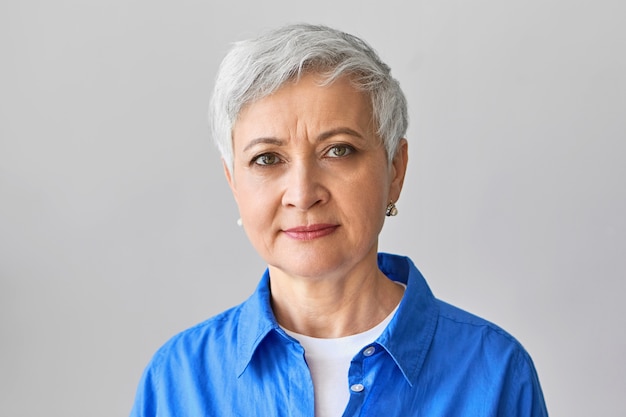 Free photo beauty, age, maturity and lifestyle concept. portrait of beautiful middle aged woman with pixie hairstyle having serious facial expression, frowning her eyebrows as if thinking about something