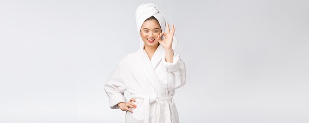 白い背景の美しさとファッションの概念に分離された良い顔の製品のための美しさのアジアの女性のokジェスチャー