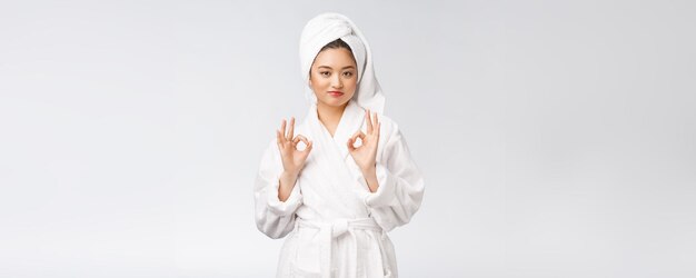 白い背景の美しさとファッションの概念に分離された良い顔の製品のための美しさのアジアの女性のokジェスチャー