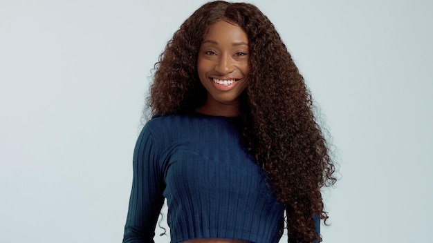 Красавица чернокожая афроамериканка смешанной расы с длинными вьющимися волосами и идеальной улыбкой смотрит в камеру и улыбается голубому