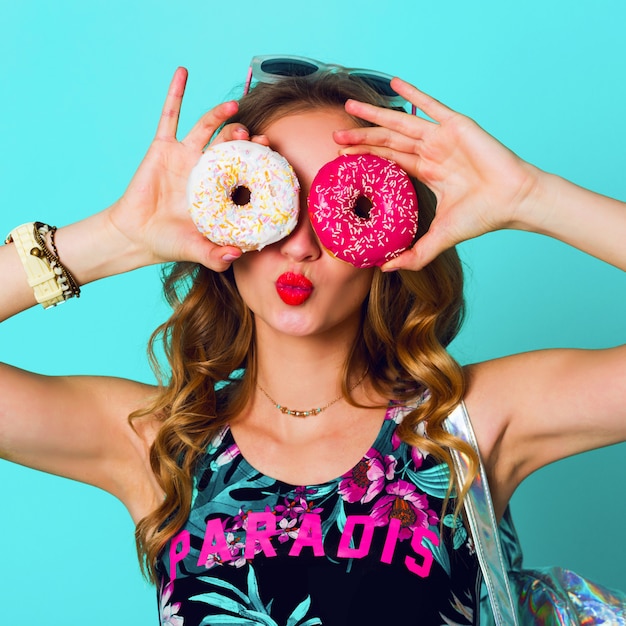 Beauty blonde  fashion model girl taking colorful pink  donuts. Funny joyful woman with sweets, dessert. Diet, dieting concept. Junk food. Bright colors.