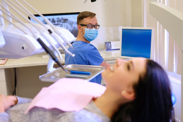 歯科医がコンピューターで作業している間待っている美ブルネットの女性。歯科医療訪問。