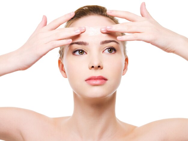 Beauty caucasian young woman applying Moisturizer cream on the forehead  - isolated on white