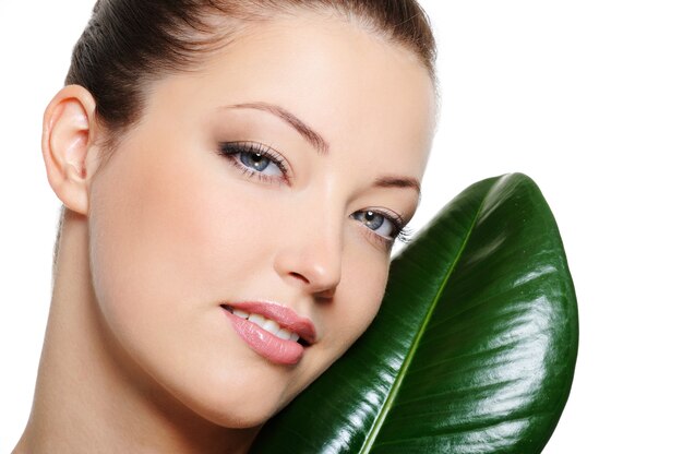 Beauty clear woman face near green leaf over white background