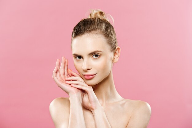 美容の概念 - きれいな新鮮な皮膚を持つ美しい女性は、ピンクのスタジオに閉じます。スキンケアの顔。化粧品。