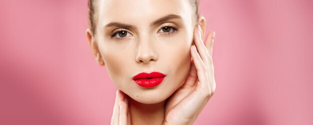 Beauty concept Close up Gorgeous Young Brunette Woman face portrait Beauty Model Girl with bright eyebrows perfect makeup red lips touching her face Isolated on pink background