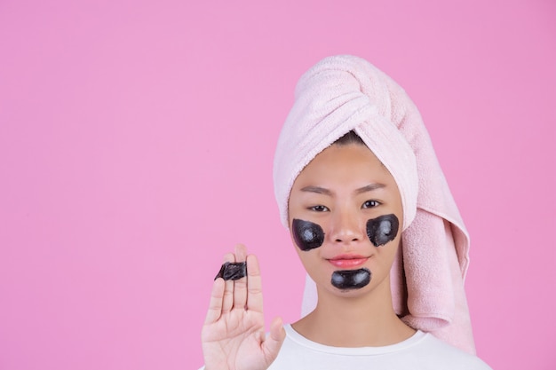 Beauty cosmetic peeling. Young female with black peel off mask on skin cosmetic skin care peeling product on face on a pink .