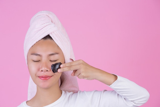 Beauty cosmetic peeling. Young female with black peel off mask on skin cosmetic skin care peeling product on face on a pink .