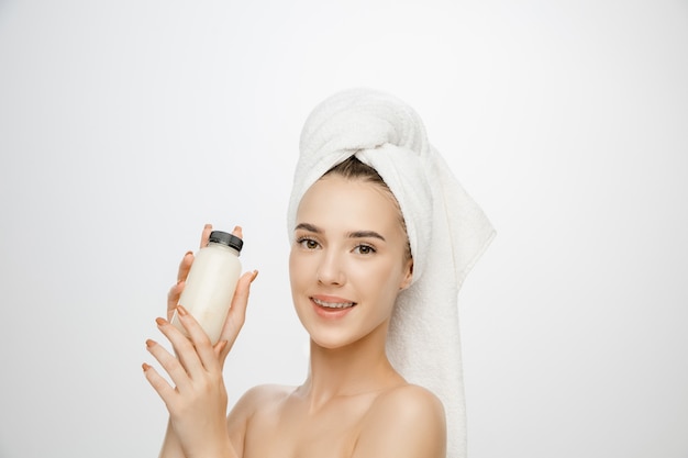 Beauty Day. Woman wearing towel on white studio wall with bottle.