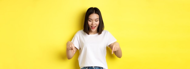 Beauty and fashion concept beautiful asian woman in white tshirt pointing fingers down demonstrate l