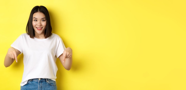 Beauty and fashion concept beautiful asian woman in white tshirt pointing fingers down demonstrate l