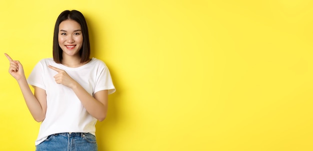 Free photo beauty and fashion concept beautiful asian woman in white tshirt pointing fingers left standing over