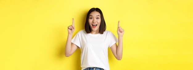 Beauty and fashion concept beautiful asian woman in white tshirt pointing fingers up standing over y