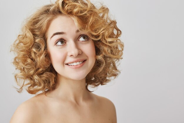 Beauty and fashion concept. Dreamy curly-haired girl with naked shoulders smiling, looking upper right corner