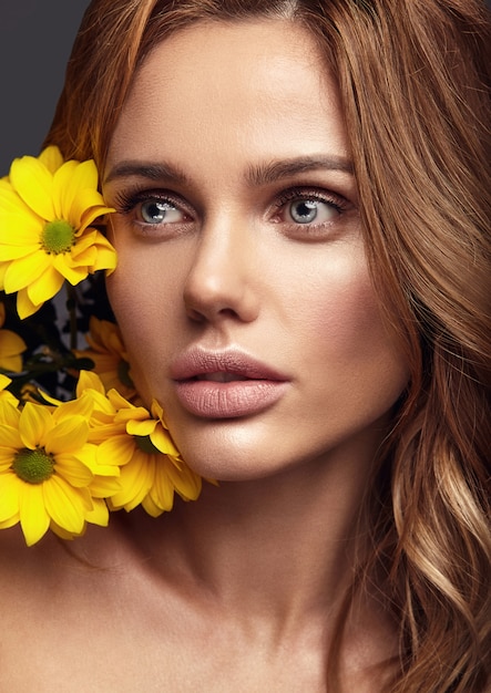 Beauty fashion portrait of young blond woman model with natural makeup and perfect skin with bright yellow chrysanthemum flower posing