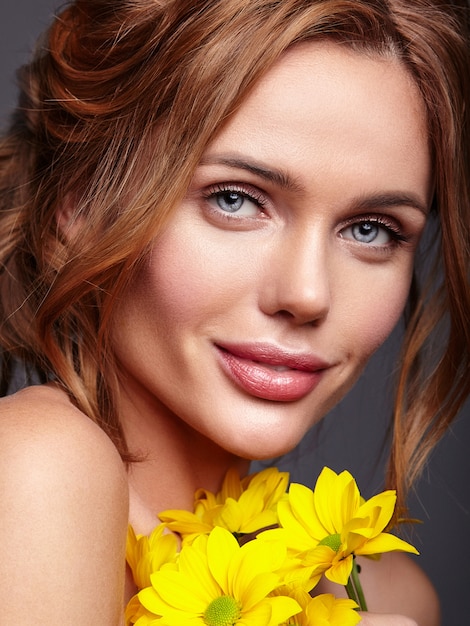 Beauty fashion portrait of young blond woman model with natural makeup and perfect skin with bright yellow chrysanthemum flower posing