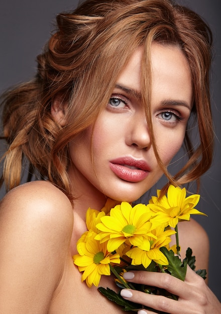 Beauty fashion portrait of young blond woman model with natural makeup and perfect skin with bright yellow chrysanthemum flower posing
