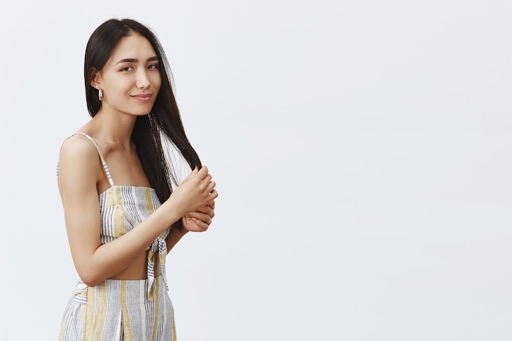 무료 Photo 미용, 헤어 스타일 및 헤어 케어 개념. 깨끗한 피부, 머리카락을 만지고 부드러운 미소로 응시하는 부드러운 매력적인 젊은 여성의 초상화, 회색 벽 위에 서서