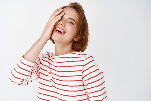 Beauty Happy attractive woman with short hair covering half of face and laughing with candid cheerful emotions standing against white background