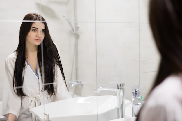 Beauty, hygiene, morning and people concept. smiling young woman looking to mirror at home bathroom