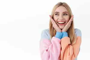 Free photo beauty lifestyle and fashion concept closeup portrait of dreamy tender attractive blonde girl touching her face and smiling as looking away at promo announcement stand white background