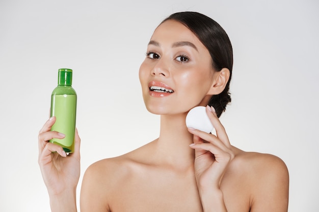 Beauty and morning hygiene of young woman with soft healthy skin cleaning face with lotion and cotton pad, isolated over white