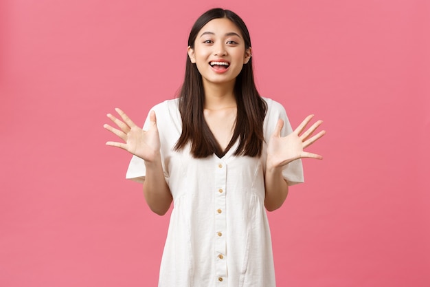 Beauty, people emotions and summer leisure concept. Excited glamour pretty asian girl describe awesome news, gesturing, raising hands and smiling as tell big announcement, pink background.