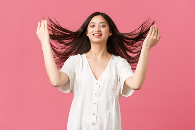 Beauty, people emotions and summer leisure and vacation concept. Sensual and tender asian woman bragging with hair haircut, show-off hair after haircare products or salon, pink background