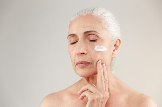 Beauty portrait of an attractive half naked elderly woman holding lipstick and posing