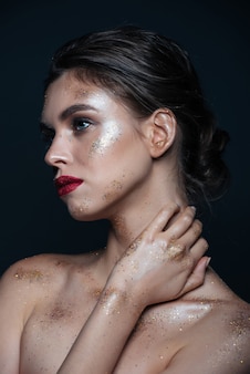 Beauty portrait of attractive young woman with sparkling makeup touching her neck over black surface