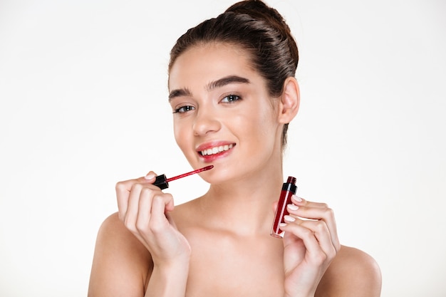 Beauty portrait of caucasian brunette woman with hair in bun applying lip gloss looking