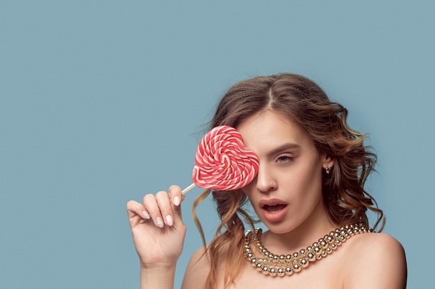 Beauty portrait of a cute girl in act to eat a candy over blue studio