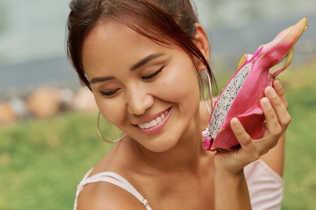 Beauty portrait of graceful Asian model with perfect skin holding dragon fruits near face.