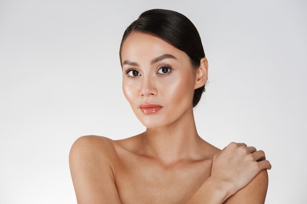 Beauty portrait of half-naked woman looking on camera and touching her gentle shoulder, isolated over white