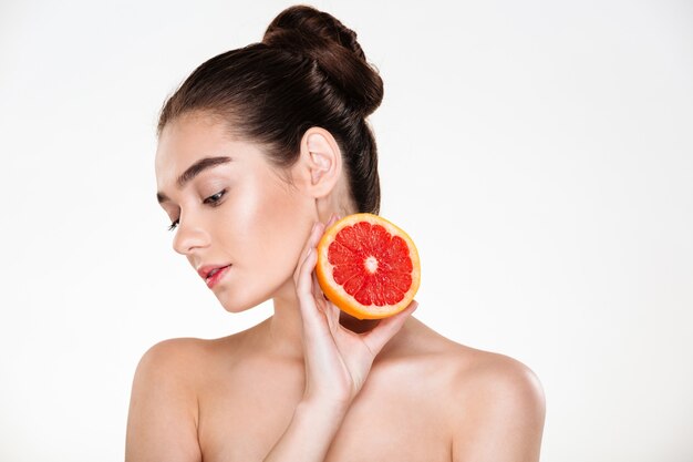 Красота портрет довольно женственной женщины с мягкой кожей, держа сочный грейпфрут возле ее шеи, с удовольствием