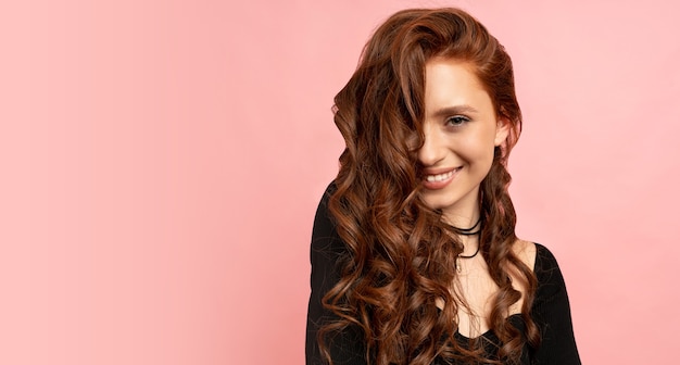 Beauty portrait of red head woman posing over pink wall. wavy hairs. perfect smile.